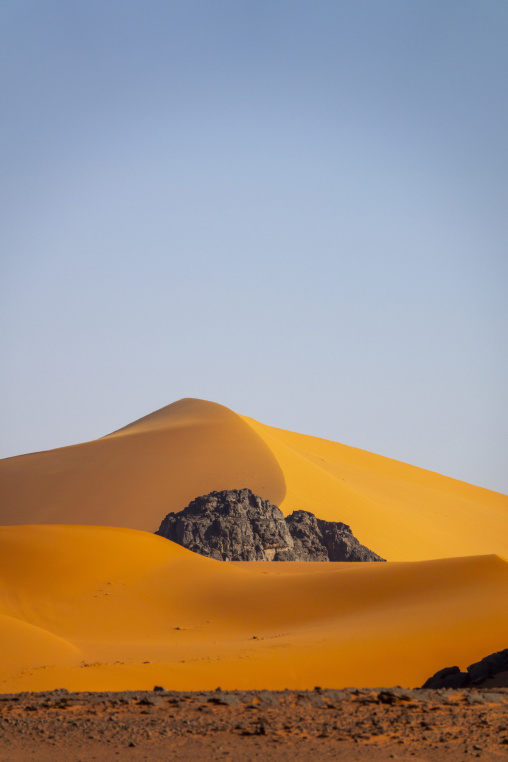 Rocky outcrop emerging from a golden sand dune beneath a clear sky, Tassili N'Ajjer National Park, Tadrart Rouge, Algeria