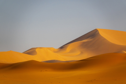 Layered golden sand dunes beneath a pale blue sky in the Sahara desert, Tassili N'Ajjer National Park, Tadrart Rouge, Algeria