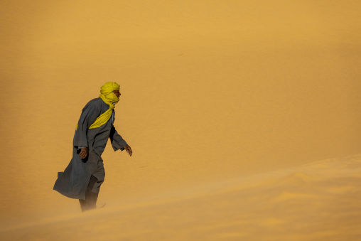 Tuareg man walking in a sandstorm, North Africa, Erg Admer, Algeria