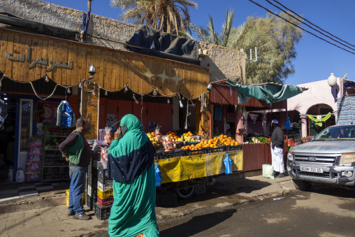Woman in a green haik buying oranges at a street market, North Africa, Djanet, Algeria