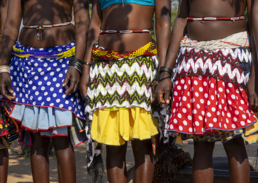 Three women in colorful patterned skirts and beaded belts stand together holding hands, Cunene Province, Cahama, Angola