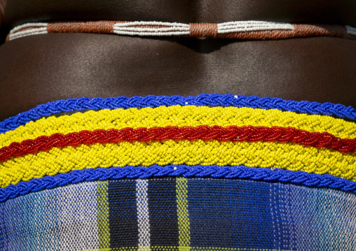Macro view of a striped beaded belt in blue yellow and red resting above a plaid skirt, Cunene Province, Cahama, Angola