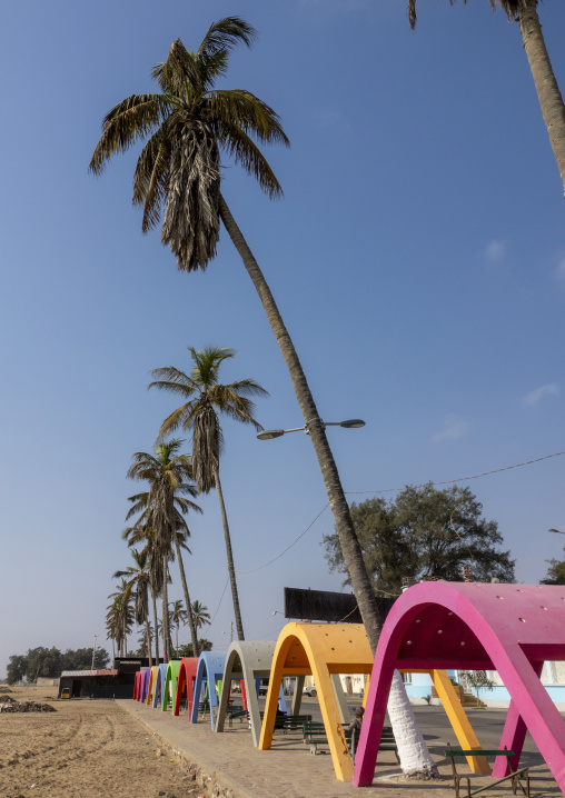 Row of colorful arched beach shelters lining the sandy shore beneath tall palm trees, Namibe Province, Namibe, Angola