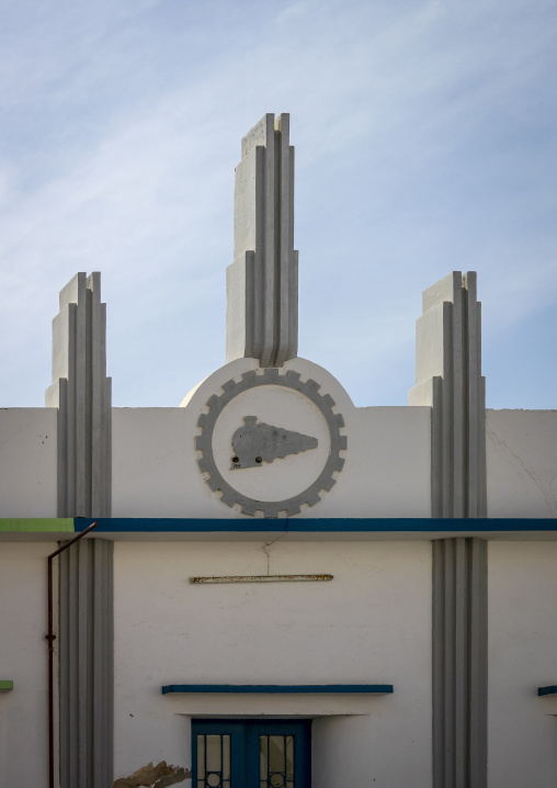 White Art Deco facade decorated with a gear and locomotive emblem above a doorway, Namibe Province, Namibe, Angola