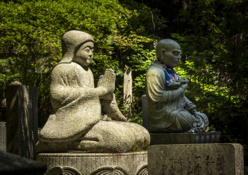 Two moss-covered stone statues of praying monks in Koyasan cemet