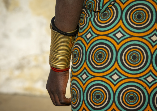 Close-up of a Mwila woman's forearm stacked with brass rings beside a circle-patterned dress, Huila Province, Lubango, Angola