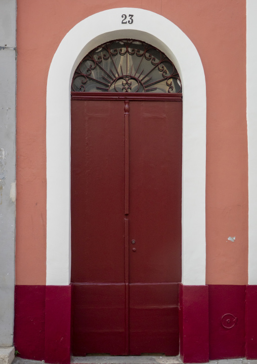 Sunburst wrought-iron fanlight tops a dark red door on a pink colonial facade, Luanda Province, Luanda, Angola