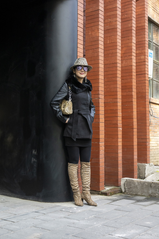 A woman poses in a leopard print outfit against a brick wall, Qinghai Province, Wayaotai, China