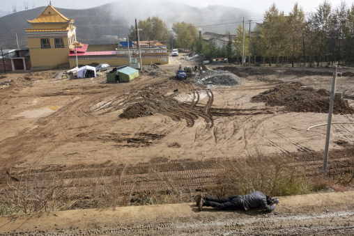 A Tibetan Buddhist pilgrim prostrates on the muddy kora path at Shachong monastery, Qinghai Province, Wayaotai, China