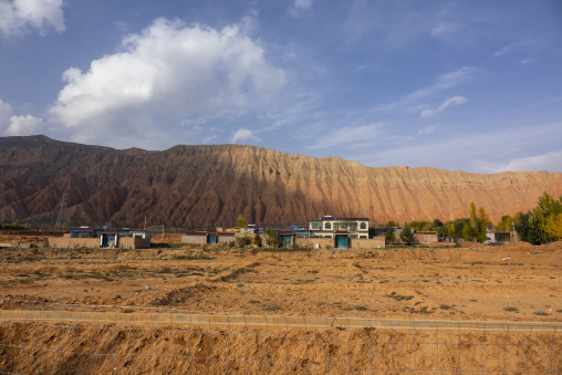 Village houses stand at the foot of red sandstone mountains, Qinghai Province, Xunhua, China