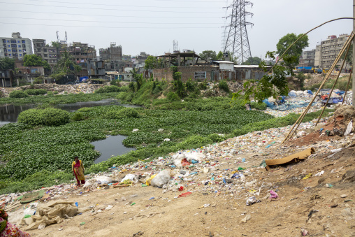 Woman standing beside a polluted river bank covered in plastic w