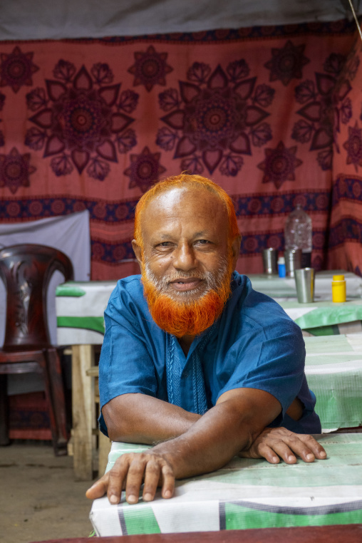 Portrait of a man with a henna-dyed orange beard sitting at a te