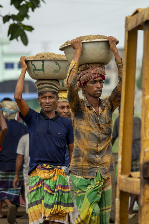 Two laborers carrying metal bowls of sand on their heads at a ri