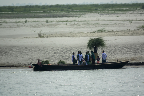 Schoolgirls and villagers boarding a wooden boat on a river sand
