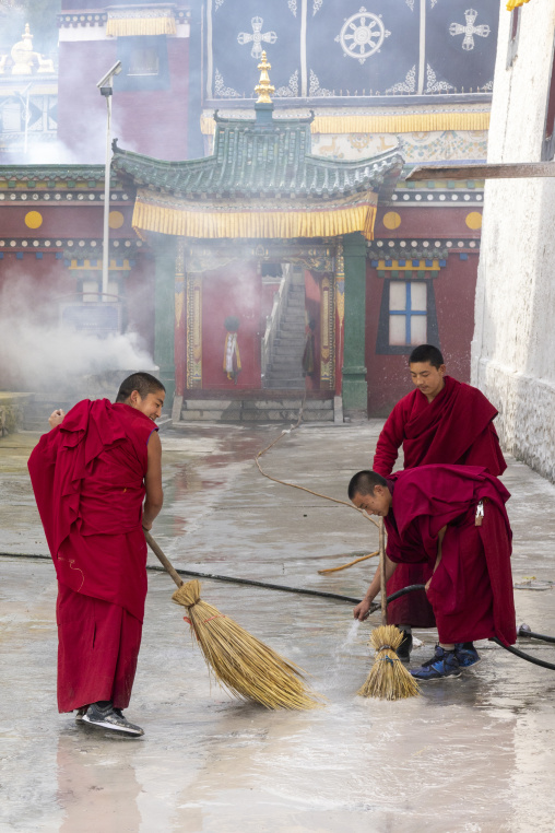 Buddhist monks in red robes sweep the courtyard of Rongwo monastery, Tongren County, Longwu, China