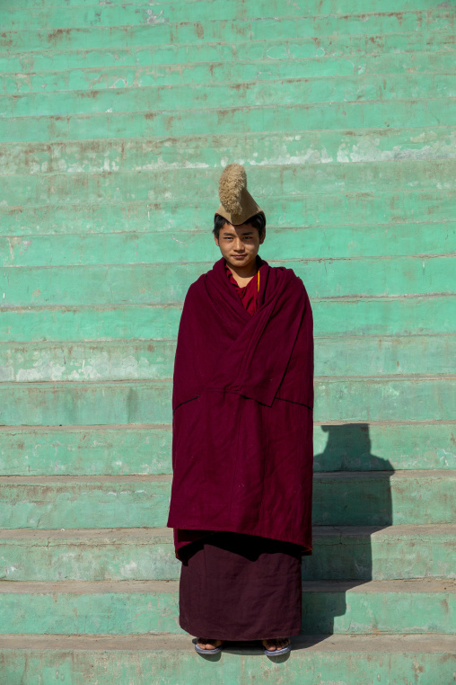 A young Tibetan monk of the Gelug or Yellow Hat sect wears a traditional hat on the steps of Bongya monastery, Qinghai Province, Mosele, China