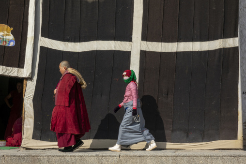 A Buddhist monk and a young woman walk past a decorated prayer tent at Labrang monastery, Gansu Province, Labrang, China