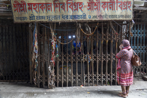Woman praying with folded hands outside a gated roadside Hindu s