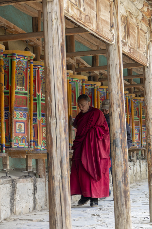 Tibetan Buddhist monk walks past prayer wheels at Labrang monastery, Gansu Province, Labrang, China