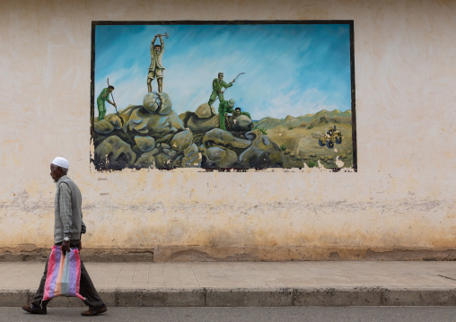 Eritrean man pssing in front of a propaganda mural about the war with ethiopia, Semien-Keih-Bahri, Keren, Eritrea