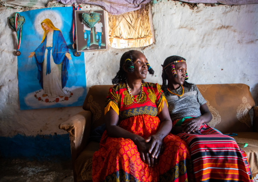 Portrait of Kunama tribe women with traditional hairstyles in front of a virgin mary poster, Gash-Barka, Barentu, Eritrea