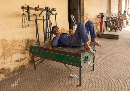 Eritrean man resting on a weighing scale in the grain market, Central region, Asmara, Eritrea