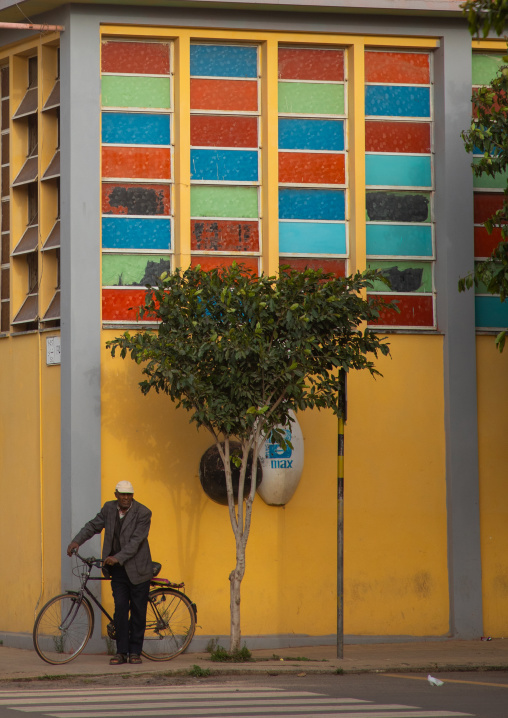 Old eritrean man with his bicycle in front of the multi sport bowling building, Central region, Asmara, Eritrea