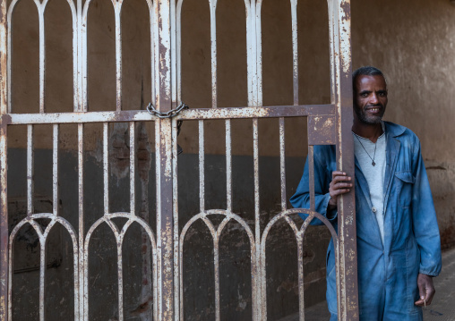 Eritrean man standing at the iron gate of an old art deco building from the italian colonial times, Central region, Asmara, Eritrea