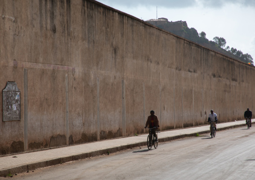 Eritrean men riding bicycles along a high wall in the street, Central region, Asmara, Eritrea