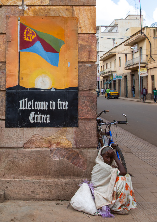 Eritrean woman sit below a propaganda billboard, Central region, Asmara, Eritrea