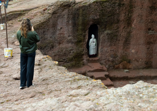European tourist taking a picture of a woman praying in a rock-hewn church, Amhara Region, Lalibela, Ethiopia