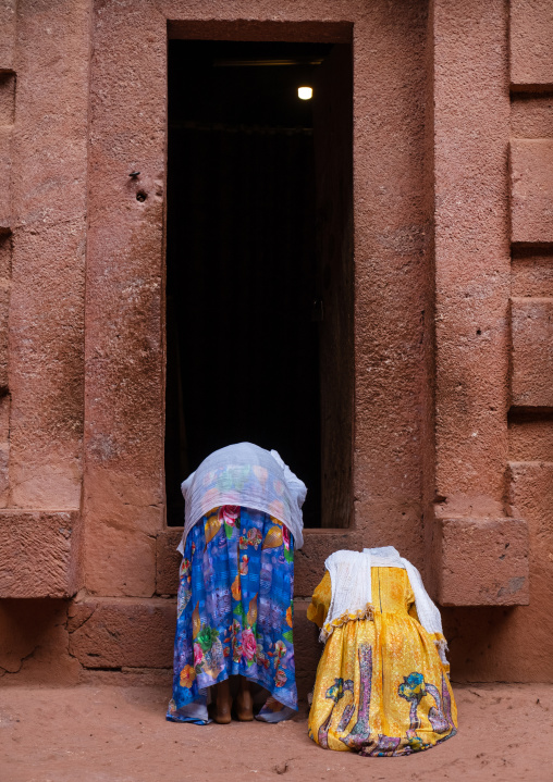 Ethiopain women bending in front of a rock-hewn church, Amhara Region, Lalibela, Ethiopia