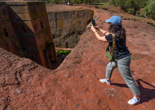 European tourist taking picture of St Georges rock-hewn church from the top, Amhara Region, Lalibela, Ethiopia