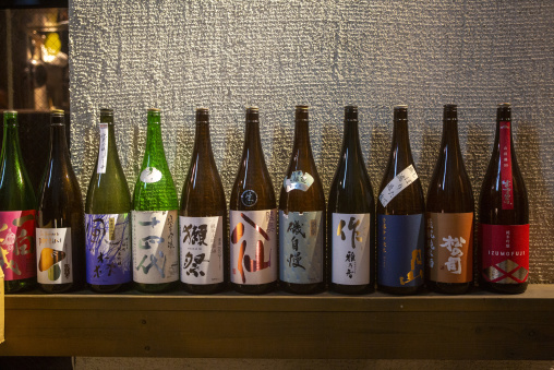 Rows of Japanese sake bottles displayed on a wooden shelf, Kansa