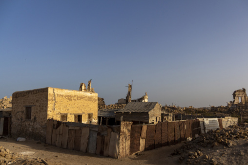 Ruined stone buildings stand behind a corrugated metal fence at sunset, Red Sea State, Suakin, Sudan