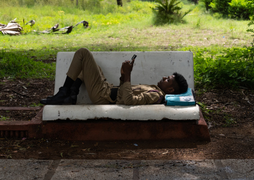 Indian soldier texting on his mobile phone on a bench in a park, Pondicherry, Puducherry, India