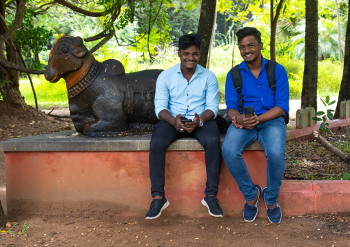Indian friends sit in a park near a cow statue, Pondicherry, Puducherry, India