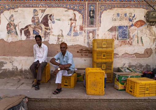 Indian men sit in front of an old mural depicting horses and elephants, Rajasthan, Nawalgarh, India