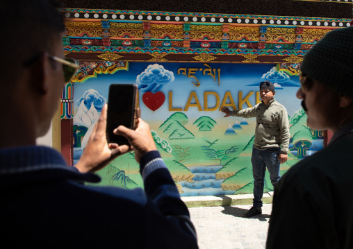 Indian men taking souvenir pictures in front of Laddakh billboard, Ladakh, Leh, India