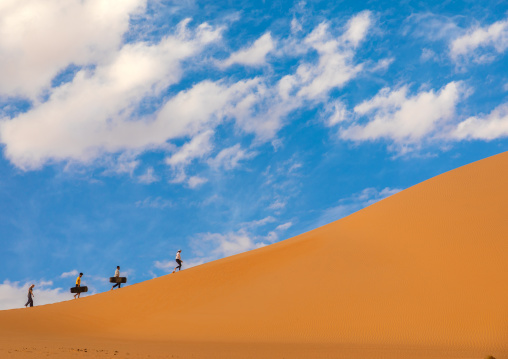 Group of friends climbing a dune to sandboard in Rub al Khali desert, Najran Province, Thar, Saudi Arabia