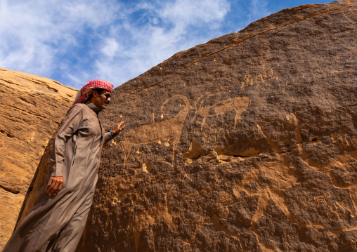 Saudi man in front off petroglyphs on a rock depicting ibex, Najran Province, Thar, Saudi Arabia