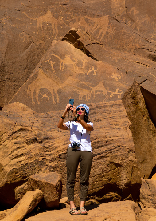 Tourist taking selfie in front of petroglyphs depicting camels, Najran Province, Thar, Saudi Arabia