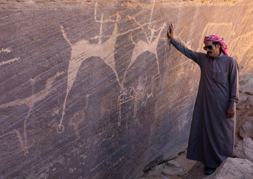 Saudi man in front of petroglyphs on a rock depicting hunters riding horses, Najran Province, Thar, Saudi Arabia