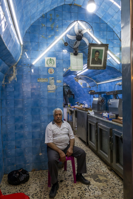 An elderly man sits on a small stool inside the blue-tiled vaulted interior of his traditional restaurant, North Governorate, Tripoli, Lebanon