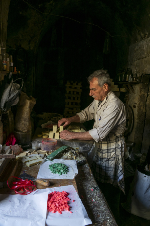 A craftsman cuts blocks of handmade soap into pieces on a wooden workbench, North Governorate, Tripoli, Lebanon