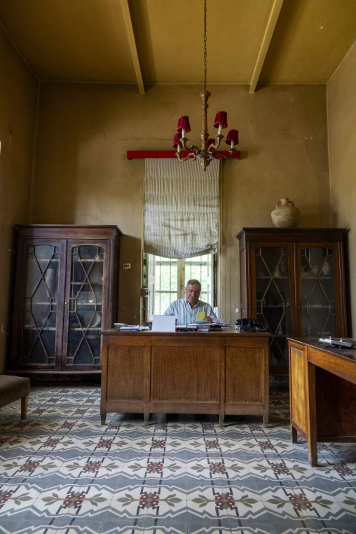 An elderly man reviews papers at an antique wooden desk inside a grand old room of the historic Palmyra Hotel, Baalbek-Hermel Governorate, Baalbek, Lebanon