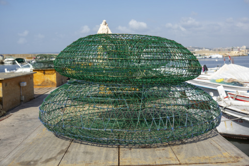 Green wire fish traps are stacked on a wooden pier overlooking the fishing harbor, South Governorate, Tyre, Lebanon