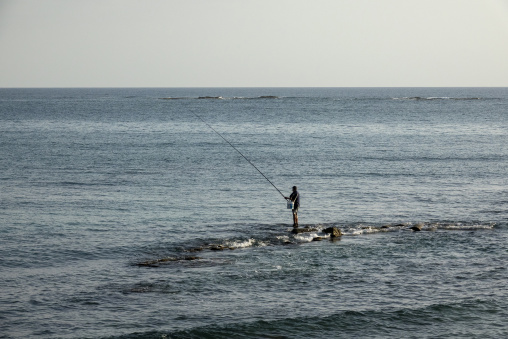 A lone fisherman casts his line from a rocky outcrop into the calm sea, South Governorate, Tyre, Lebanon