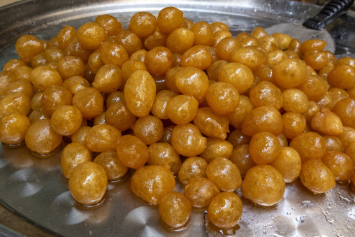 A pile of golden fried dough balls glistens with sweet syrup on a metal tray, South Governorate, Tyre, Lebanon