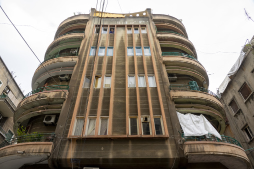 A woman looks out from a window of a curved Art Deco apartment building rising against a cloudy sky, Beirut Governorate, Beirut, Lebanon
